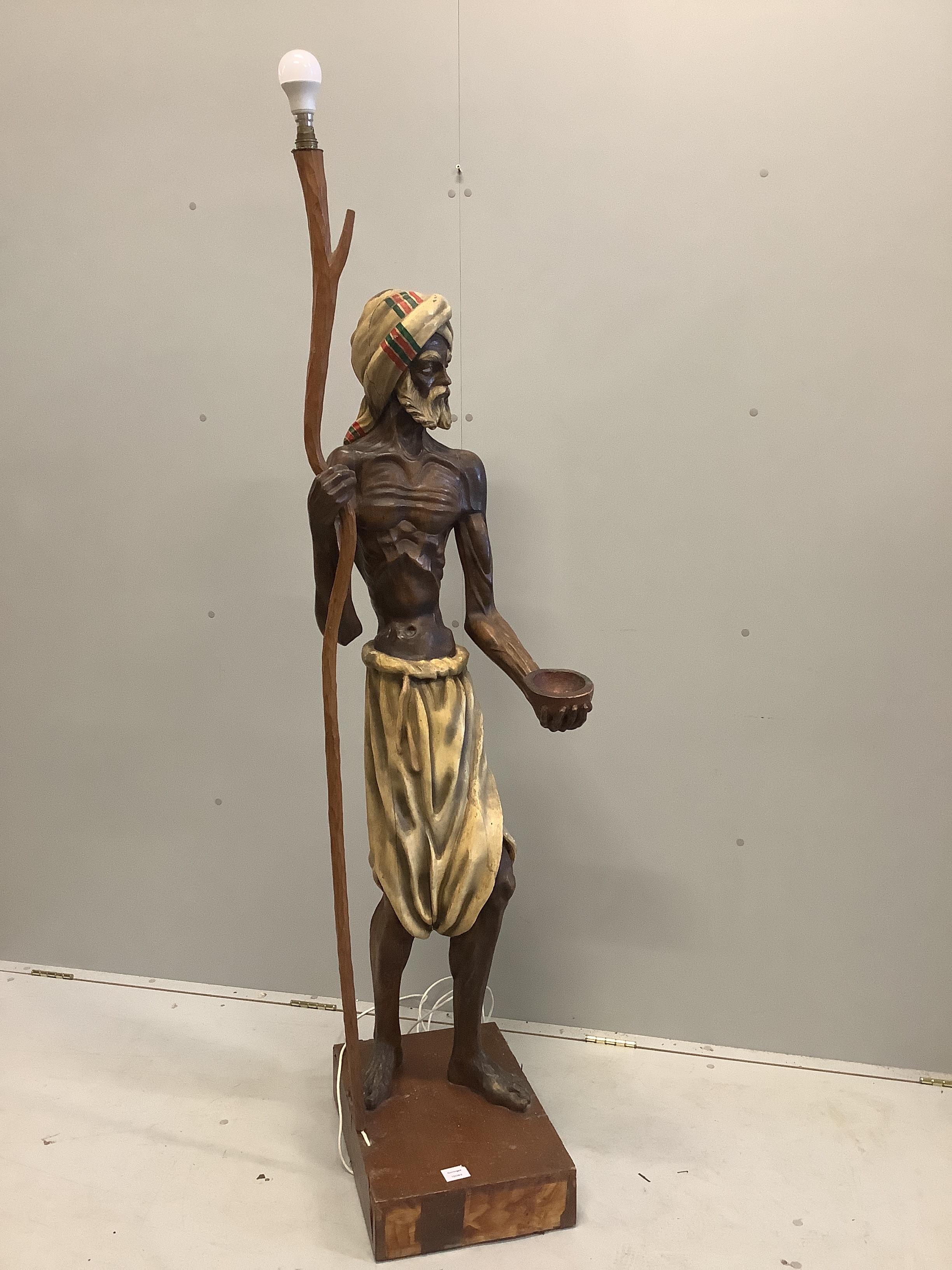 A carved wood lamp standard modelled as a beggar with a bowl and a staff, height 168cm